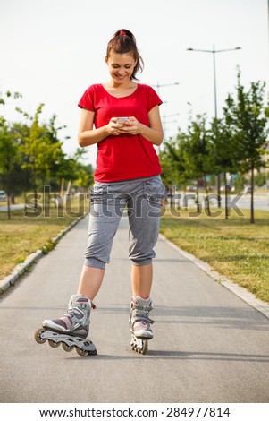 Portrait of cute young girl in roller skates using phone.Sporty girl using phone