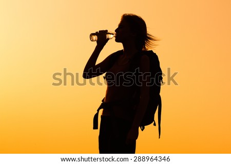 Silhouette of a woman with backpack drinking water.Refreshment for woman hiker