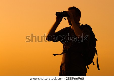 Silhouette of man watching sunset with binoculars .Hiker with binoculars