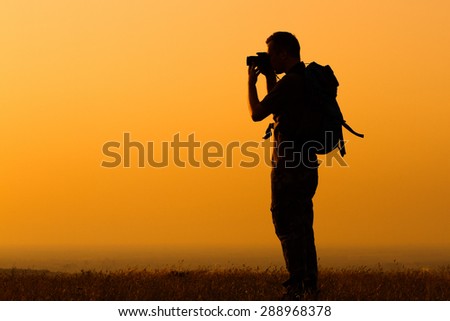 Silhouette of a man with backpack photographing.Hiker photographing