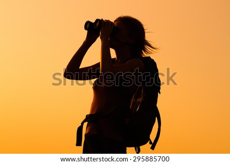 Silhouette of a woman hiker watching sunset with binoculars . Woman hiker with binoculars
