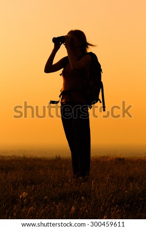 Silhouette of a woman hiker watching sunset with binoculars .Woman hiker  with binoculars