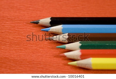 six coloured pencils over red background