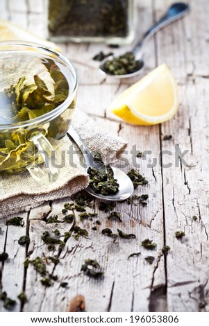 cup of green tea, spoon and lemon on rustic wooden board