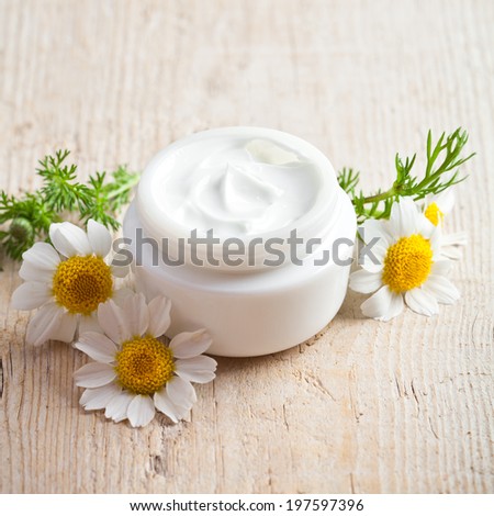 container with cream and chamomiles on wooden background