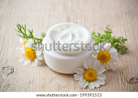 container with cream and chamomiles on wooden background