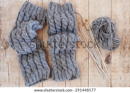 wool grey legwarmers, knitting needles and yarn on wooden background