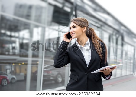 Successful businesswoman or entrepreneur using a digital tablet computer and talking on cellphone standing in front of his office.