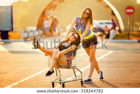 Girlfriends laughing. Girlfriends ride in a cart at the supermarket on the streets of the city.