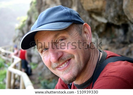 Head and shoulders of male hiker looking sideways into the camera with a baseball hat on
