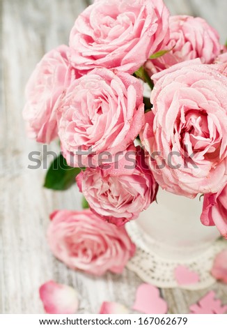 bouquet of pink roses in a vase on a painted wooden background