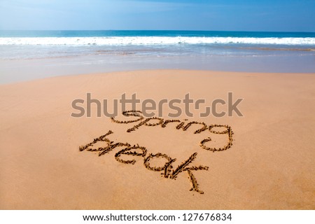 Words spring break written in sand on a tropical beach, with sea in background