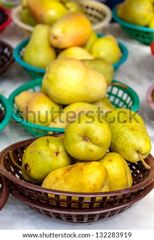 Fresh organic pears in brightly colored plastic baskets on display at farmers market
