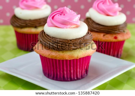 3 neapolitan frosted cupcakes on white plate with green diamond tablecloth, and pink polka background