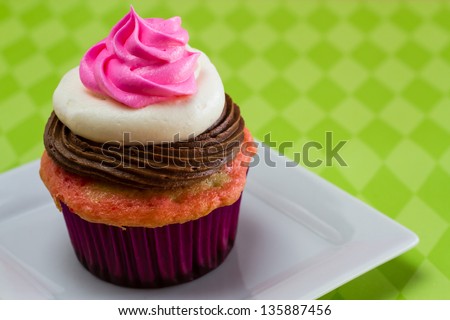 Single neapolitan frosted cupcake on white plate with green diamond tablecloth