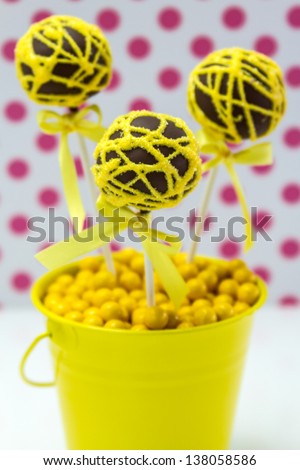 Chocolate cake pops with yellow swirl glitter sugar decorations against white background with pink polka dots, portrait orientation