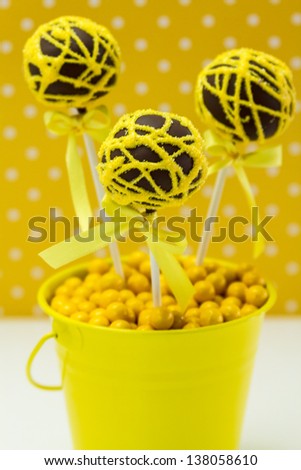 Chocolate cake pops with yellow swirl glitter sugar decorations against yellow polka dot background, portrait orientation