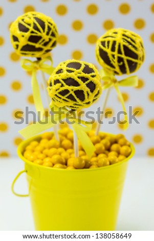 Chocolate cake pops with yellow swirl glitter sugar decorations against white background with yellow polka dots, portrait orientation