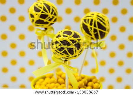 Chocolate cake pops with yellow swirl glitter sugar decorations against white background with yellow polka dots