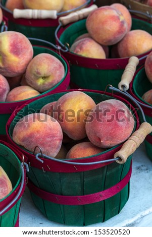 Locally grown display of fresh yellow peaches in baskets for sale at local farmers market in red baskets