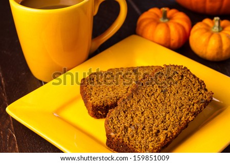 2 slices of pumpkin bread sitting on yellow square plate with mug of fresh coffee and small pumpkin gourds