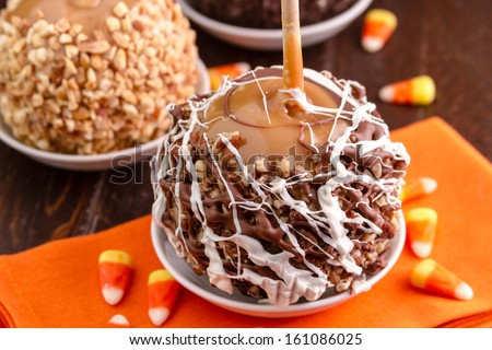 Close up of  homemade caramel apple decorated with pecans and drizzled chocolate sitting on orange napkin with candy corn
