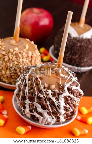Pecan and chocolate covered caramel apple sitting on orange napkin with candy corn on wooden table