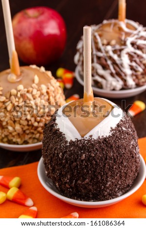 Hand dipped caramel apples decorated with cookie crumbs sitting on wooden table with orange napkin and candy corn