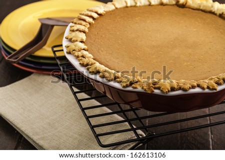 Close up of whole pumpkin pie sitting on wire baking rack with stack of colorful plates