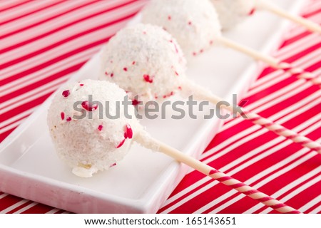 Row of peppermint brownie cake pops on white plate sitting on red striped background