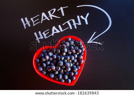 Fresh organic blueberries in red heart shaped bowl with white chalk writing on black chalkboard