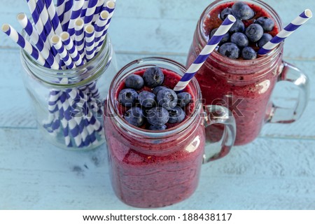 2 Mason jars filled with blueberry and blackberry fresh fruit smoothie sitting on blue wood background with straws