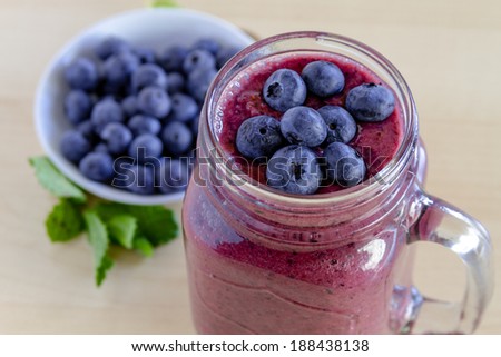 Mason jar filled with blueberry and blackberry fresh fruit smoothie sitting on counter with bowl of blueberries