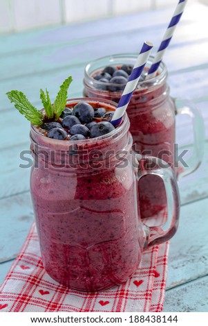 2 Mason jars filled with blueberry and blackberry fresh fruit smoothie sitting on blue wood background with straws and heart napkin
