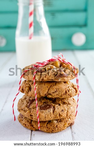 Stack of homemade chocolate chip cookies tied with red bakers twine and glass of milk with red striped straw