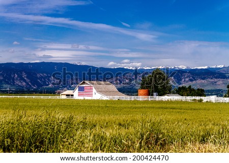 White barn with American flag painted on the side in front of growing wheat field near Rocky Mountains