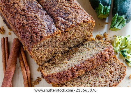 Close up of loaf of homemade zucchini bread sitting on counter with fresh zucchini squash, shreds and cinnamon sticks