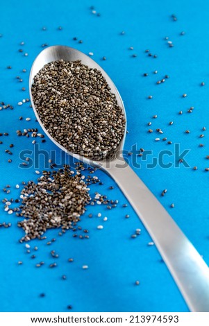 Black chia seeds on large silver spoon sitting on bright blue table top