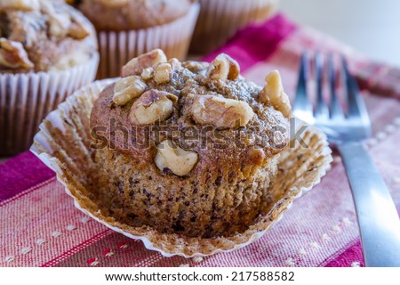 Close up of homemade banana walnut and chia seed muffin with paper removed sitting on red and brown striped napkin with fork