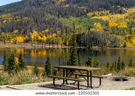 Picnic area on shore of mountain lake on warm fall afternoon with brightly colored trees changing color reflecting on water surface