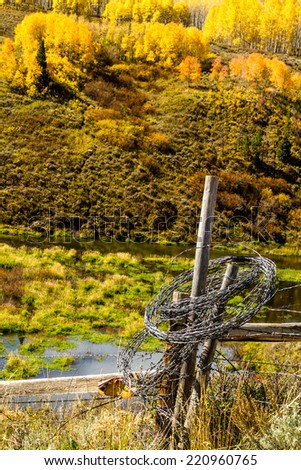 Rolled up barb wire fencing hanging on fence post in colorful mountain meadow