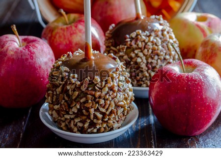 Close up of homemade caramel apples with nuts and chocolate drizzle with red apples spilling out of bushel basket