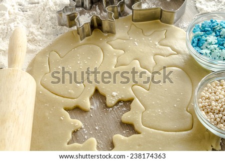 Snowflake and mitten cookie cutters cutting out holiday sugar cookies with wooden rolling pin and white dragÃ?Â?Ã?Â©e and blue snowflake candy sprinkles