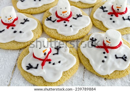 Melting snowman sugar cookies sitting on white wooden table with sparkling sugar snow