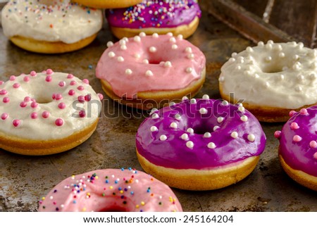 Close up of assortment of homemade vanilla bean donuts with colorful icing sitting on metal baking pan