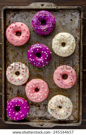 Assortment of homemade vanilla bean donuts with colorful icing sitting on metal baking pan