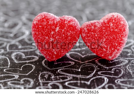 Two cinnamon heart candies coated with sugar sitting on black chalk board heart background