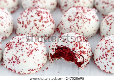 Red velvet cake balls with red sugar sprinkles sitting on white wooden table