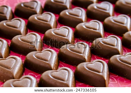 Rows of chocolate heart shaped candies filled with fudge sitting on red heart background