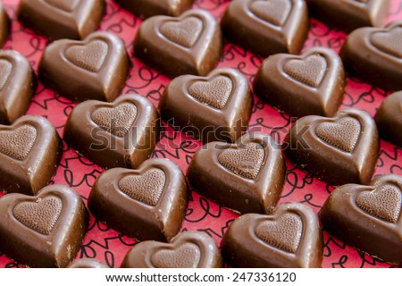 Rows of chocolate heart shaped candies filled with fudge sitting on red background with black text spelling love